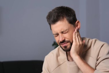 Man suffering from ear pain on in room, space for text
