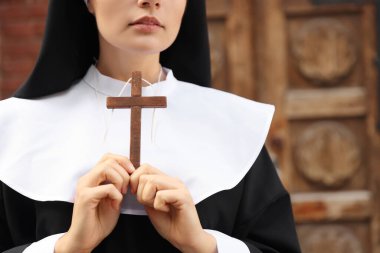 Young nun with Christian cross near old wooden door