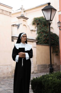 Young nun with Bible on city street