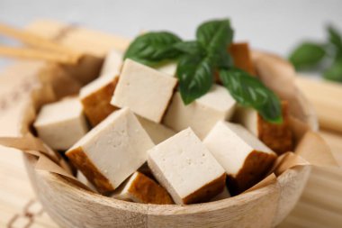 Bowl of smoked tofu cubes and basil on bamboo mat, closeup