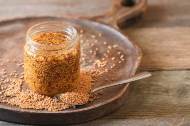 Jar and spoon of whole grain mustard on wooden table, closeup. Space for text