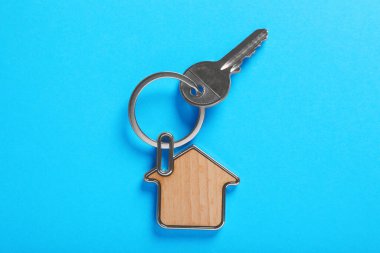 Key with trinket in shape of house on blue background, top view. Real estate agent services