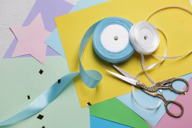 Pair of scissors with ribbons and colorful paper sheets on white wooden table, flat lay