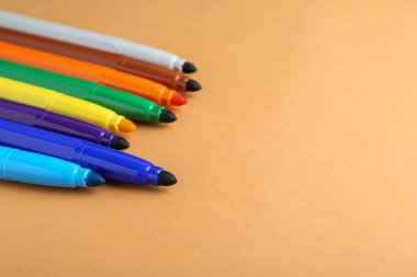 Different colorful markers on light brown background, space for text