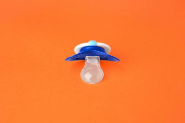 One blue baby pacifier on orange background