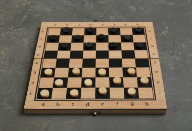 Wooden checkerboard with game pieces on grey table
