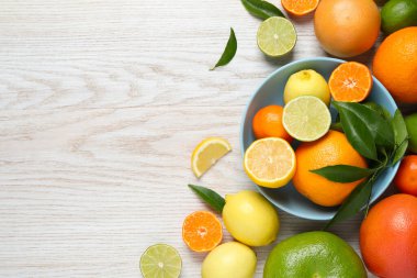 Beyaz ahşap masada yeşil yapraklı farklı olgun narenciye meyveleri var. Metin için boşluk