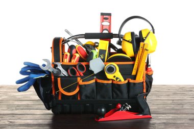 Bag with different tools on wooden table against white background