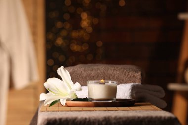 Spa composition with burning candle, lily flower and towels on massage table in wellness center, space for text