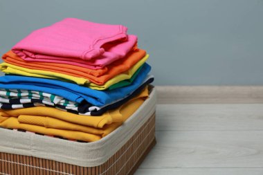 Laundry basket with clean stacked clothes on floor near grey wall, closeup. Space for text clipart