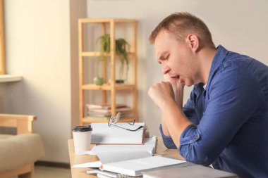 Tired man studying at wooden table indoors