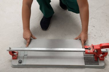 İşçi yerde elle kiremit kesici kullanıyor, yakın plan.