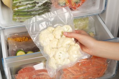 Woman putting vacuum bag with cauliflowers into fridge, closeup. Food storage clipart