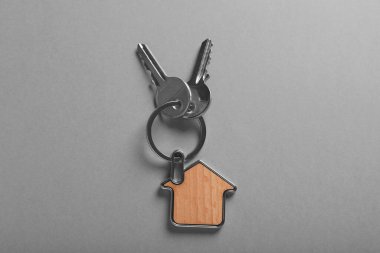 Gri arka planda ev şeklinde incik boncuklu anahtarlar, üst manzara. Emlakçılık hizmetleri