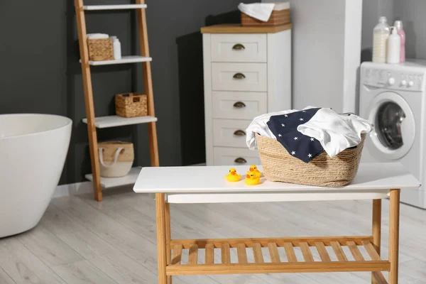 Laundry basket with baby clothes and rubber ducks on table in bathroom. Space for text