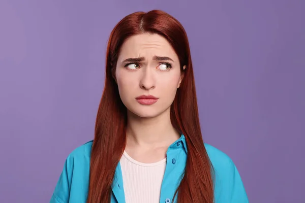 Confused woman with red dyed hair on purple background