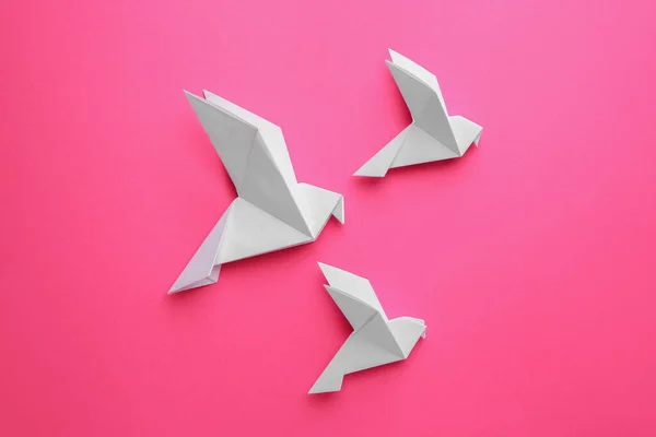 Beautiful white origami birds on pink background, flat lay