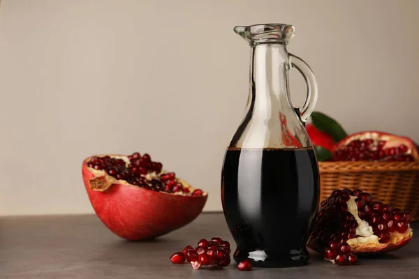 Glass jug of tasty pomegranate sauce and fresh ripe fruits on light grey table. Space for text