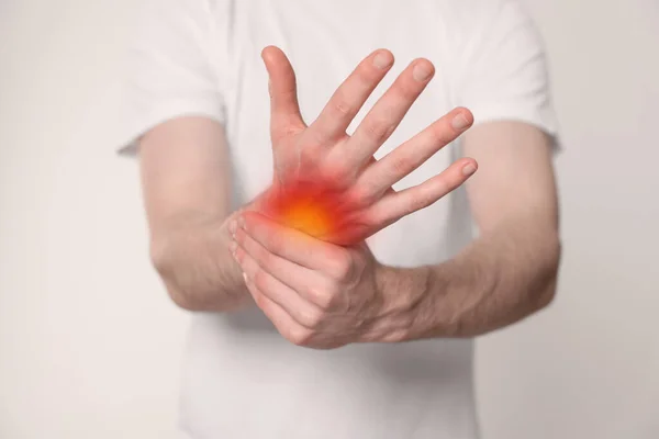 Arthritis symptoms. Man suffering from pain in his hand on light background, closeup