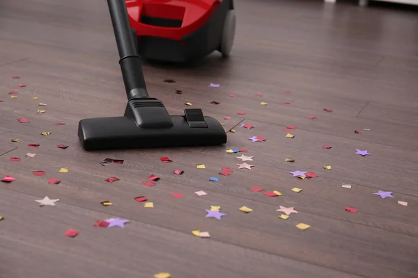Vacuuming confetti from wooden floor in room