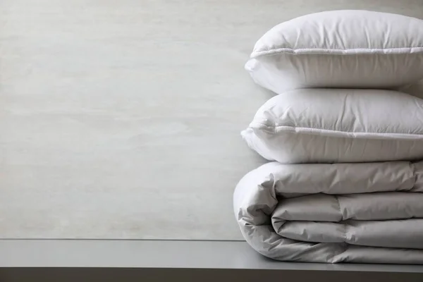 Soft folded blanket and pillows on light grey table, closeup. Space for text