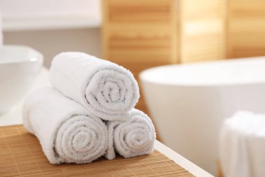 Rolled soft towels on white table in bathroom. Space for text