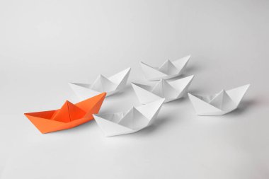 Group of paper boats following orange one on white background. Leadership concept