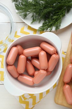 Bowl of delicious sausages and dill on white wooden table, flat lay