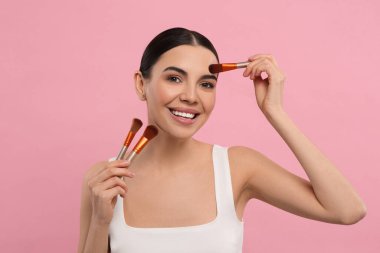 Farklı makyaj fırçalarıyla pembe arka planda mutlu bir kadın.
