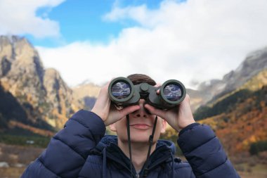 Boy looking through binoculars in beautiful mountains, closeup