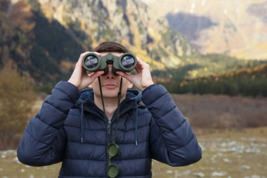 Boy looking through binoculars in beautiful mountains