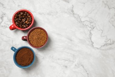 Instant, ground coffee and roasted beans in cups on white marble table, flat lay. Space for text