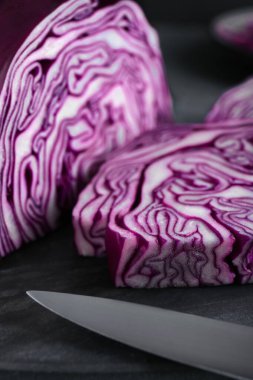 Slices of fresh ripe red cabbage and knife on grey table, closeup