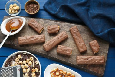 Tasty chocolate bars with caramel and nuts on light blue wooden table, flat lay