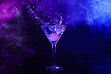 Martini splashing out of glass on table in neon lights