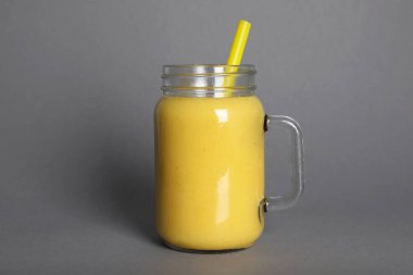 Mason jar of tasty smoothie with straw on grey background