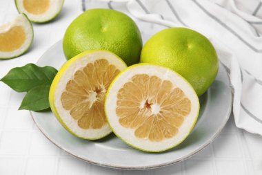 Whole and cut sweetie fruits with green leaves on white tiled table