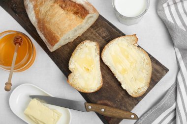 Sandwiches with butter, honey and milk on white table, flat lay