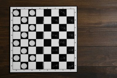 Checkerboard with game pieces on wooden table, top view. Space for text