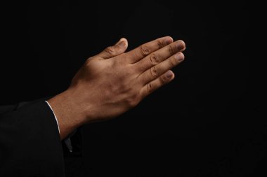 African American man praying to God on black background, closeup of hands