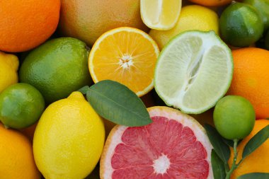 Different fresh citrus fruits and leaves as background, top view.