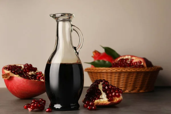 Glass jug of tasty pomegranate sauce and fresh ripe fruits on light grey table