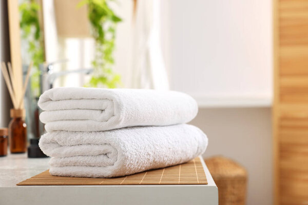 Stacked soft towels on white table in bathroom. Space for text