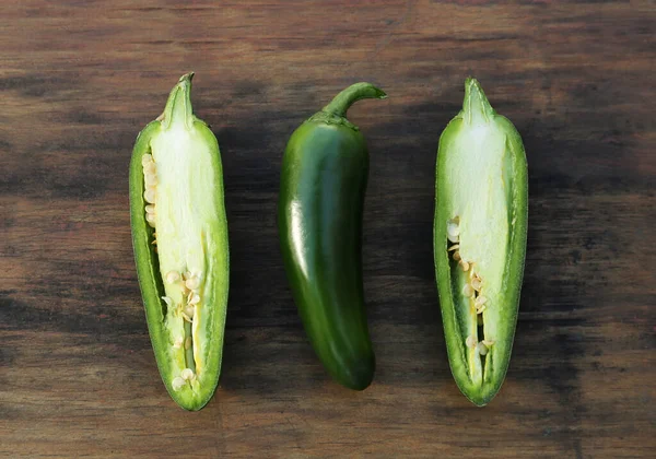 Whole and cut green chili peppers on wooden table, flat lay