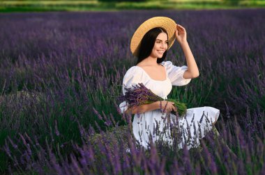 Beautiful young woman with bouquet sitting in lavender field