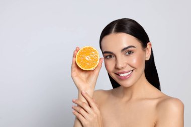 Woman holding half of orange on light grey background, space for text. Spa treatment