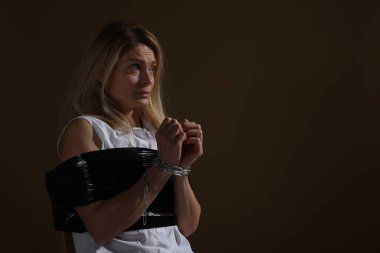 Scared woman taped up and taken hostage on dark background. Space for text