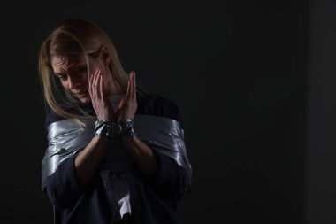 Scared woman taped up and taken hostage on dark background. Space for text