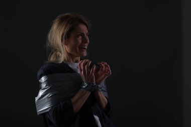 Scared woman taped up and taken hostage on dark background. Space for text