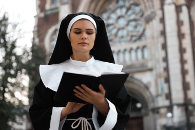 Young nun reading Bible near cathedral outdoors